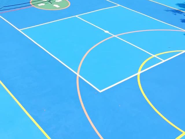 Cancha deportiva pintada de azul, con líneas blancas, naranjas y amarillas, obra de INMCOM.